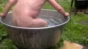 Naked old man rolls around in outside bath tub.